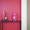 Aap beeldje roze op een wandtafel naast een geurstokjeshouder