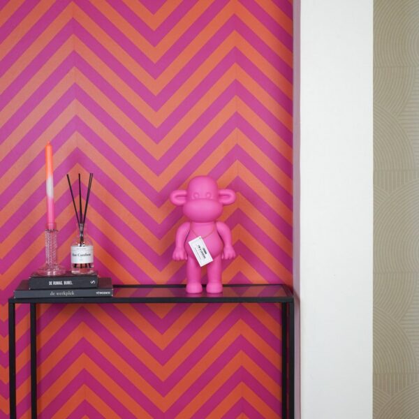 Aap beeldje roze op een wandtafel naast een geurstokjeshouder